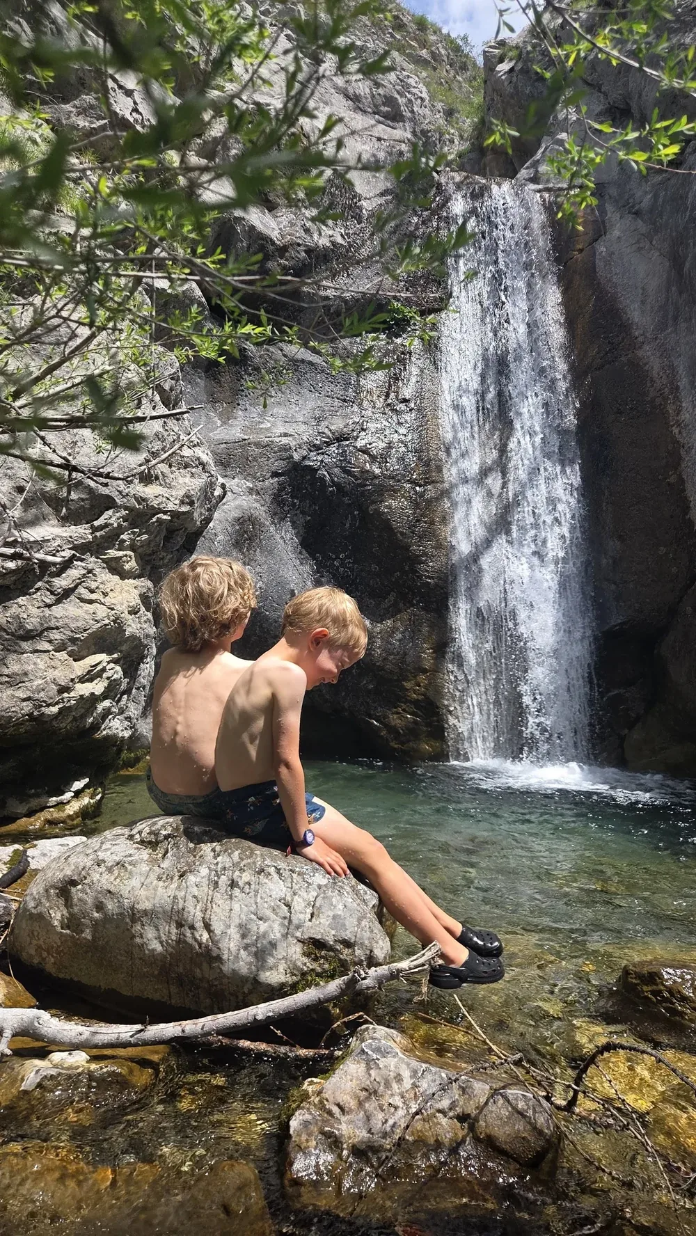 Nos deux garçons de dos, assis sur un rocher, contemplant une cascade.