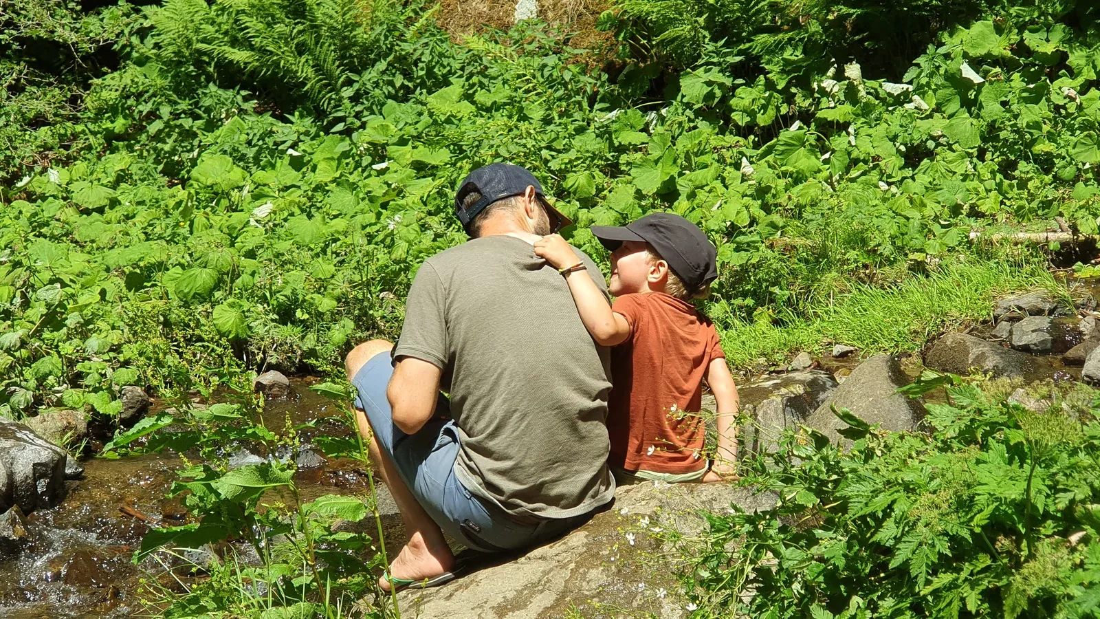 Le plus petit, au bord d'un ruisseau, levant les yeux vers son papa, une main posée sur son épaule.