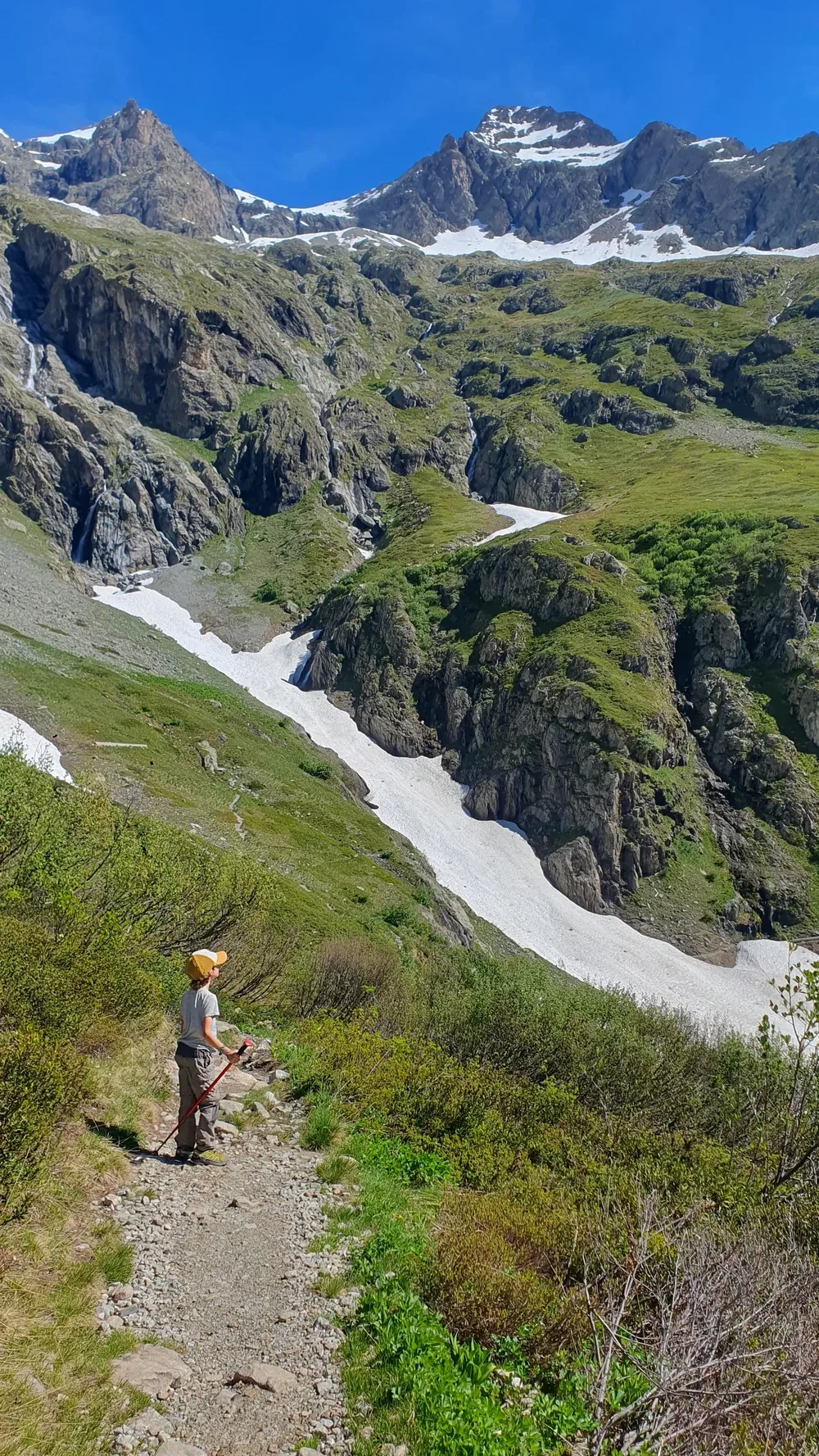 Un de nos garçons en pause sur un sentier de montagne, face aux sommets enneigés des Alpes.
