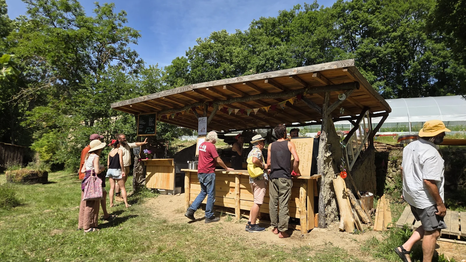 Buvette en bois du festival sous un auvent, avec des visiteurs qui patientent