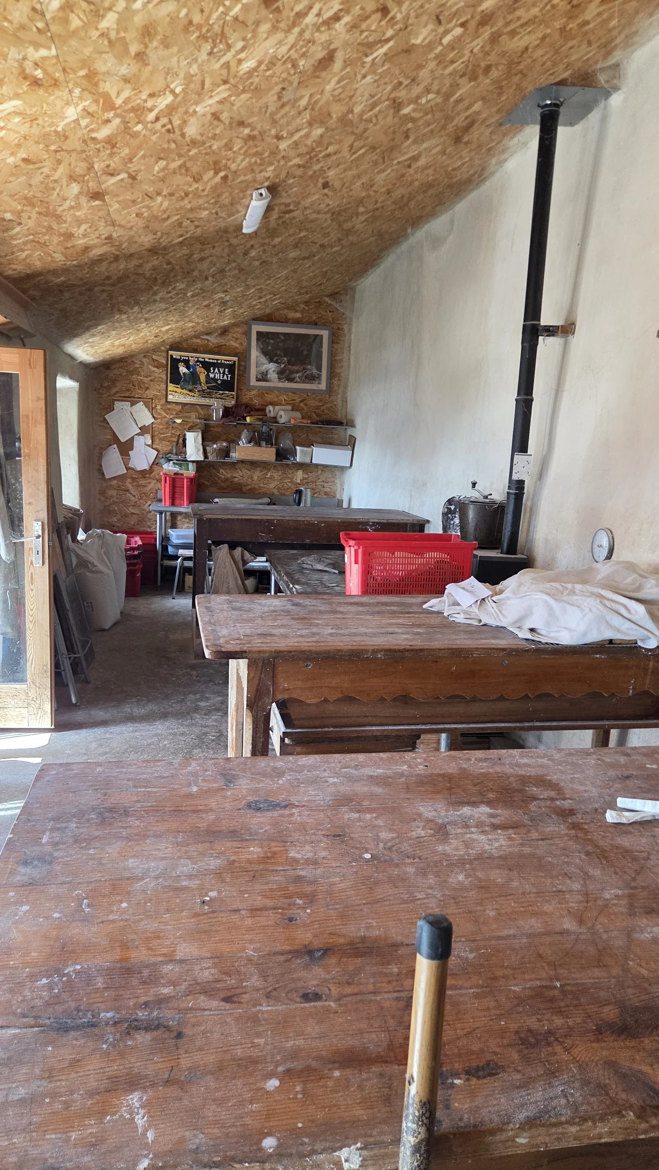 Intérieur du fournil : grande table en bois farinée, bannetons et toiles de lin, pétrin contre le mur
