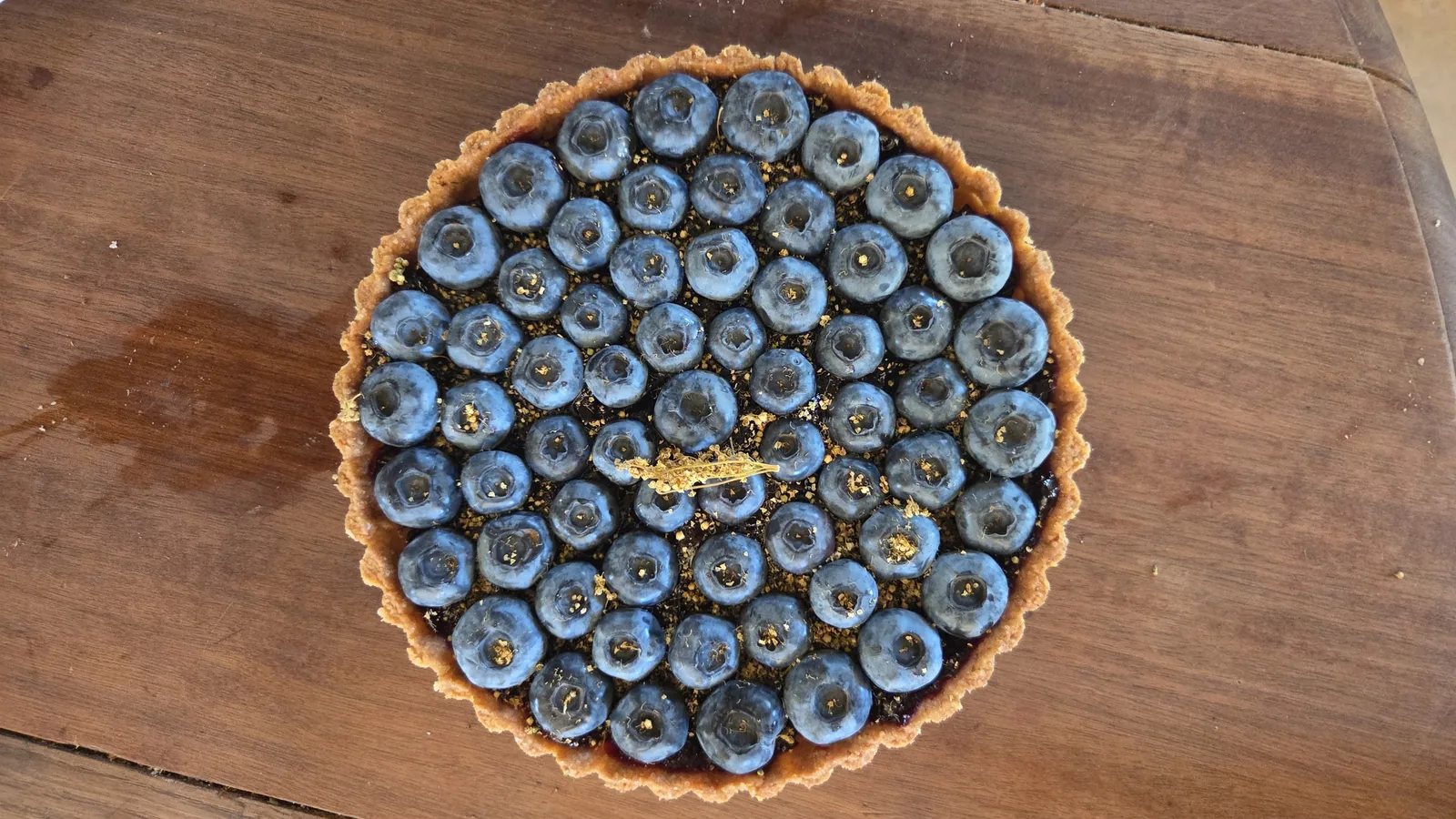 Une tarte aux myrtilles fraîchement cueillies, posée sur une table en bois ronde, vue du dessus