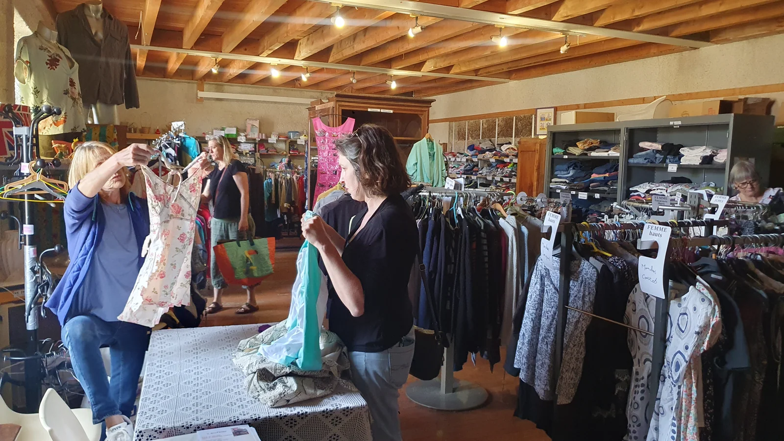 Plusieurs personnes trient des vêtements sur des portants dans la donathèque du Monastier
