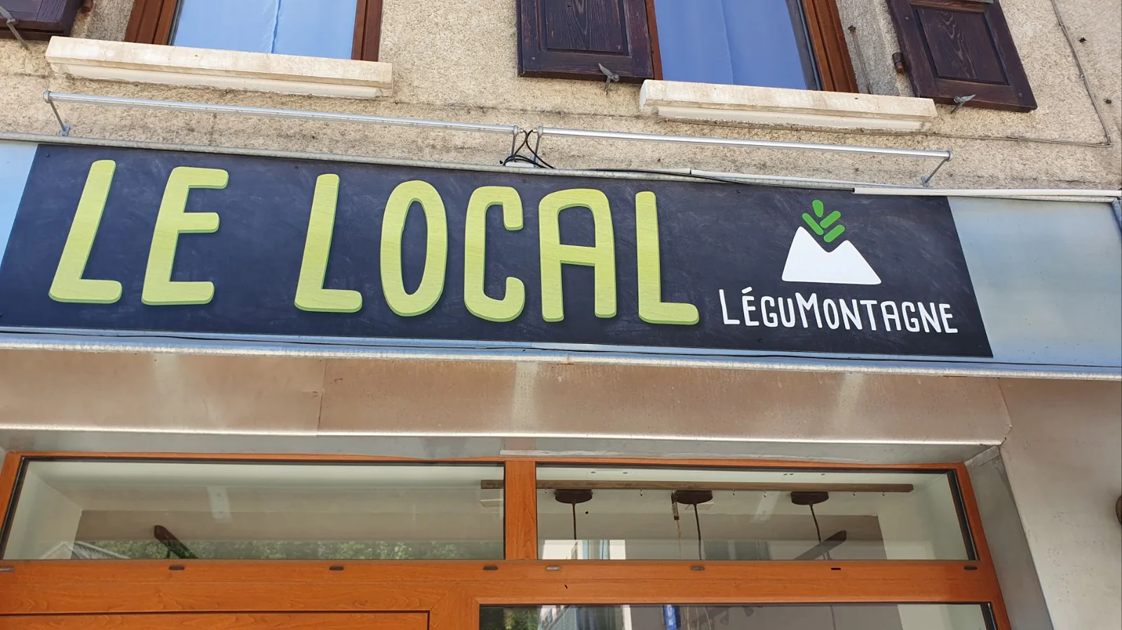 Enseigne du magasin sur une façade : « LE LOCAL » en grandes lettres vertes, avec le logo LéguMontagne représentant une montagne et une pousse