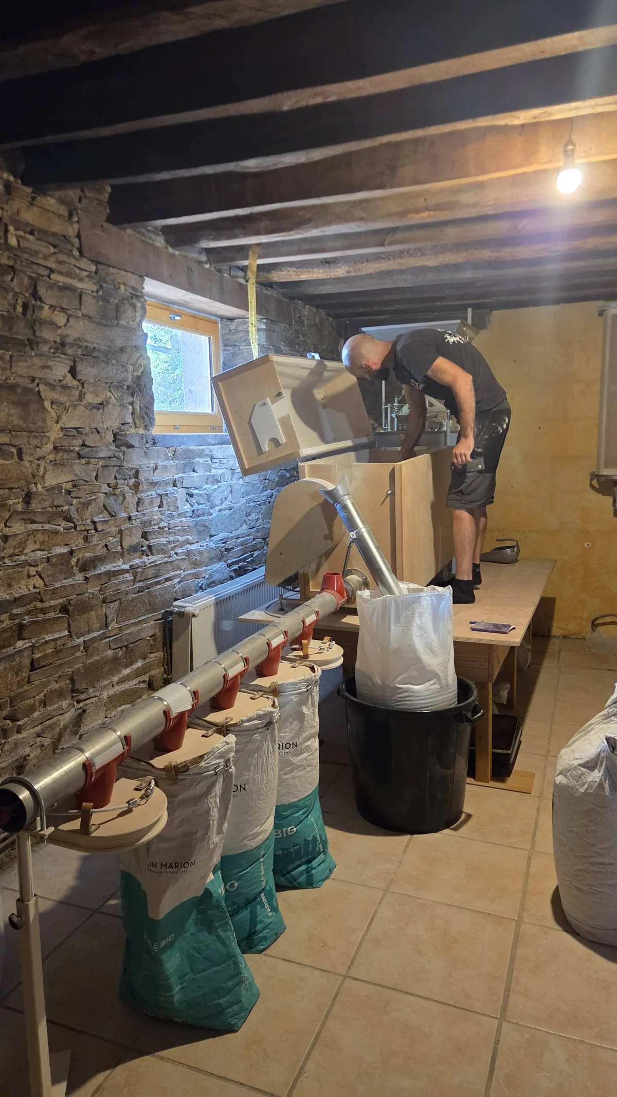 Damien au moulin Astrié, la farine descendant dans les sacs alignés au sol contre le mur de pierre