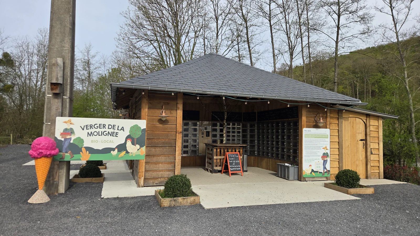 Façade en bois du magasin du Verger de la Molignée, distributeurs visibles à l'intérieur, enseigne peinte et grosse glace décorative à l'extérieur